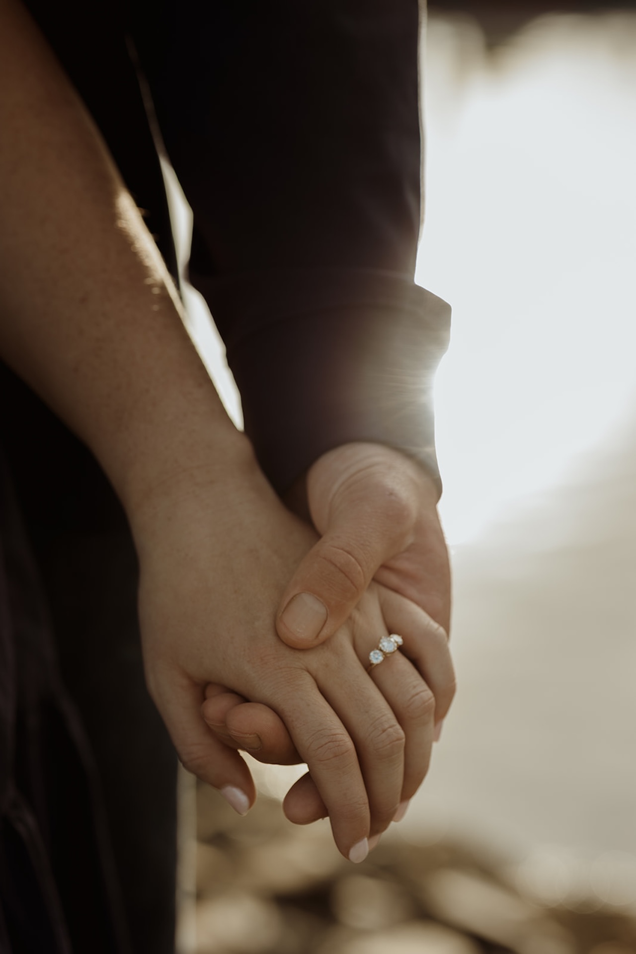 Close-up detail of couple holding hands with engagement ring sparkling in warm golden hour light.