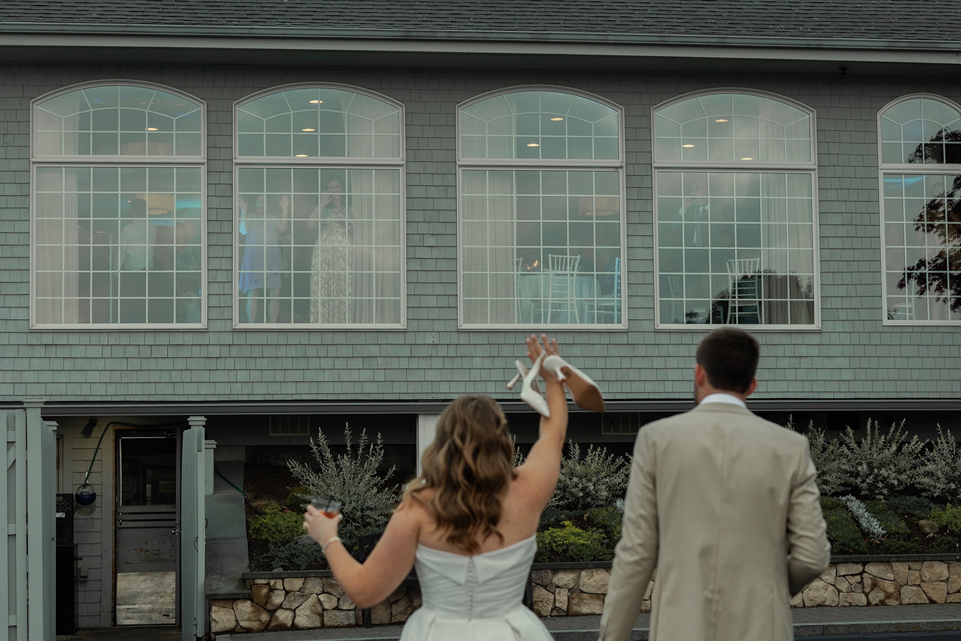 Newlyweds walking outside waving to guests through reception windows at Stage Neck Inn.