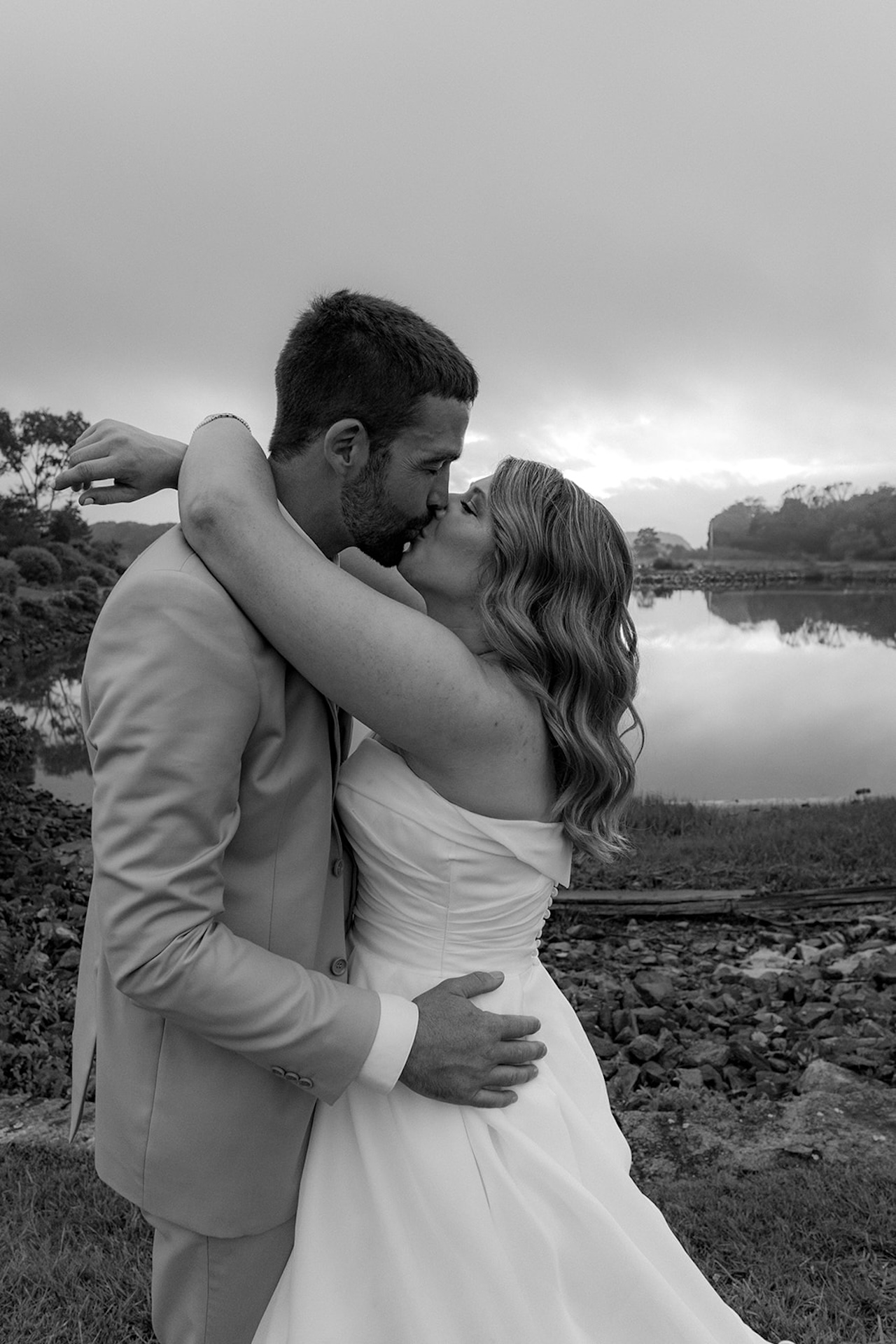 Bride and groom kissing by the water during a foggy coastal sunset portrait on their wedding day.
