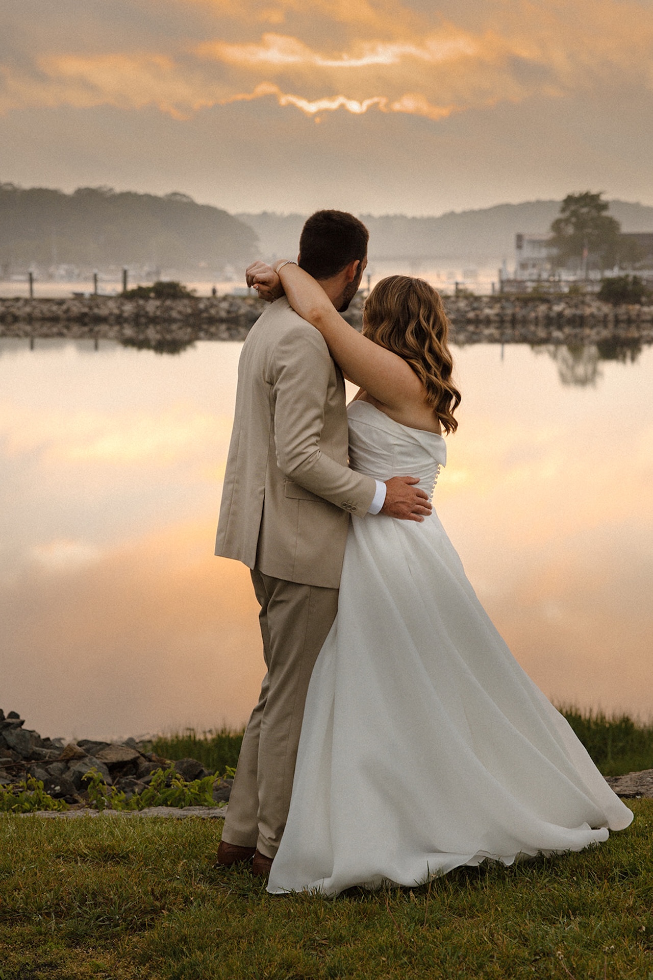 Bride and groom embracing while watching the sunset over the water on their wedding day.
