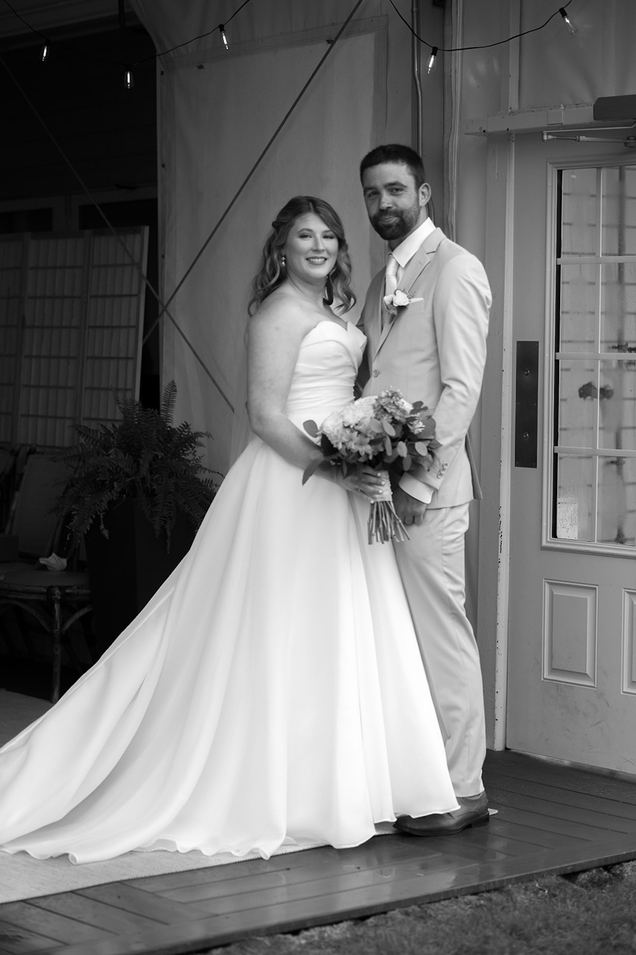 Bride and groom posing together on a covered porch in black and white on their wedding day.