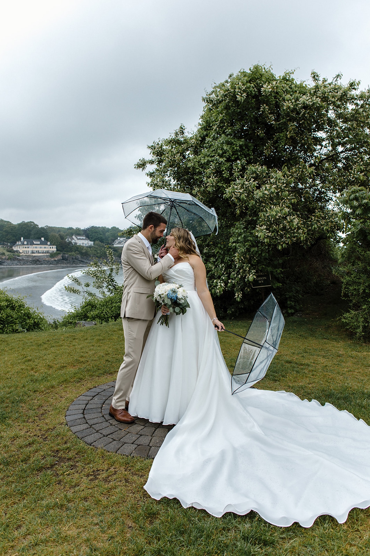 Bride and groom sharing an intimate moment under umbrellas on the rainy lawn at Stage Neck Inn in Maine.