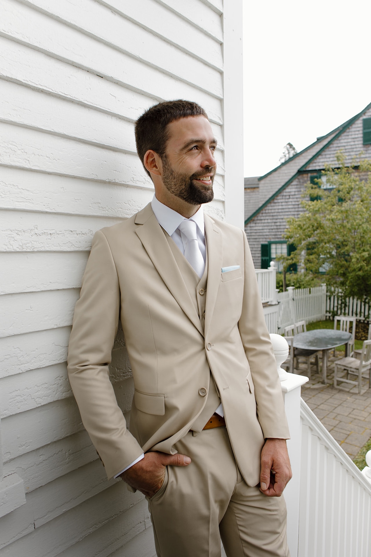 Groom portrait in a tan suit leaning against white coastal siding at Stage Neck Inn wedding venue.