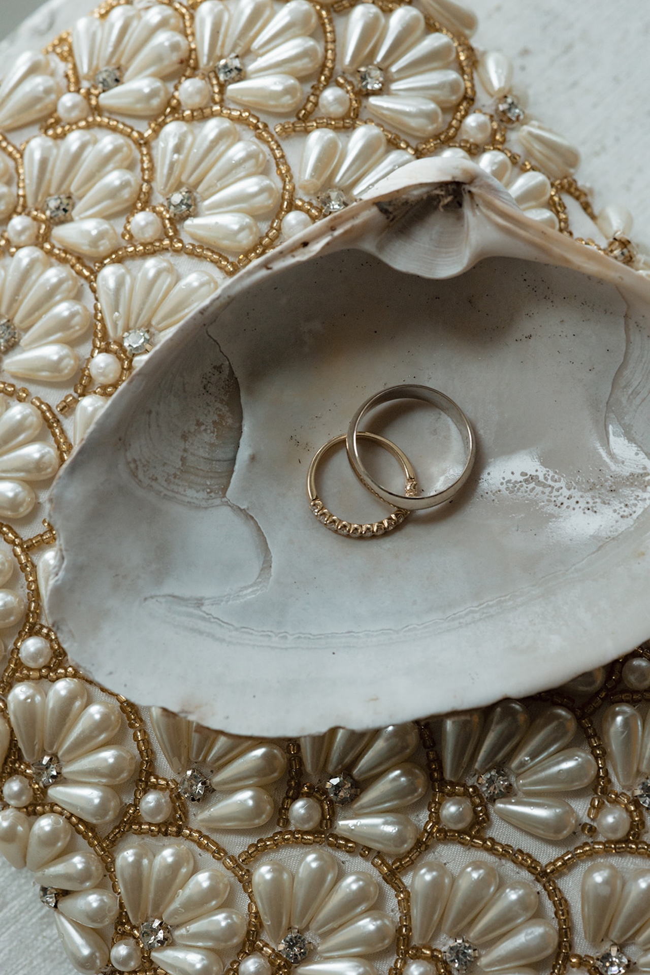 Wedding rings styled inside a seashell on pearl beaded fabric for coastal wedding details.