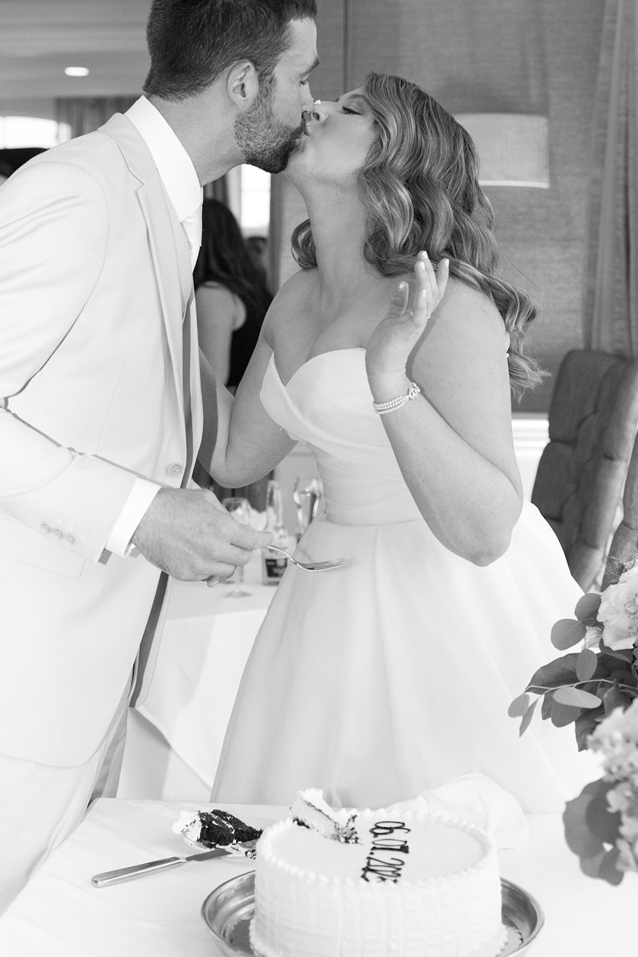 Bride and groom sharing a kiss while holding cake during their wedding reception.