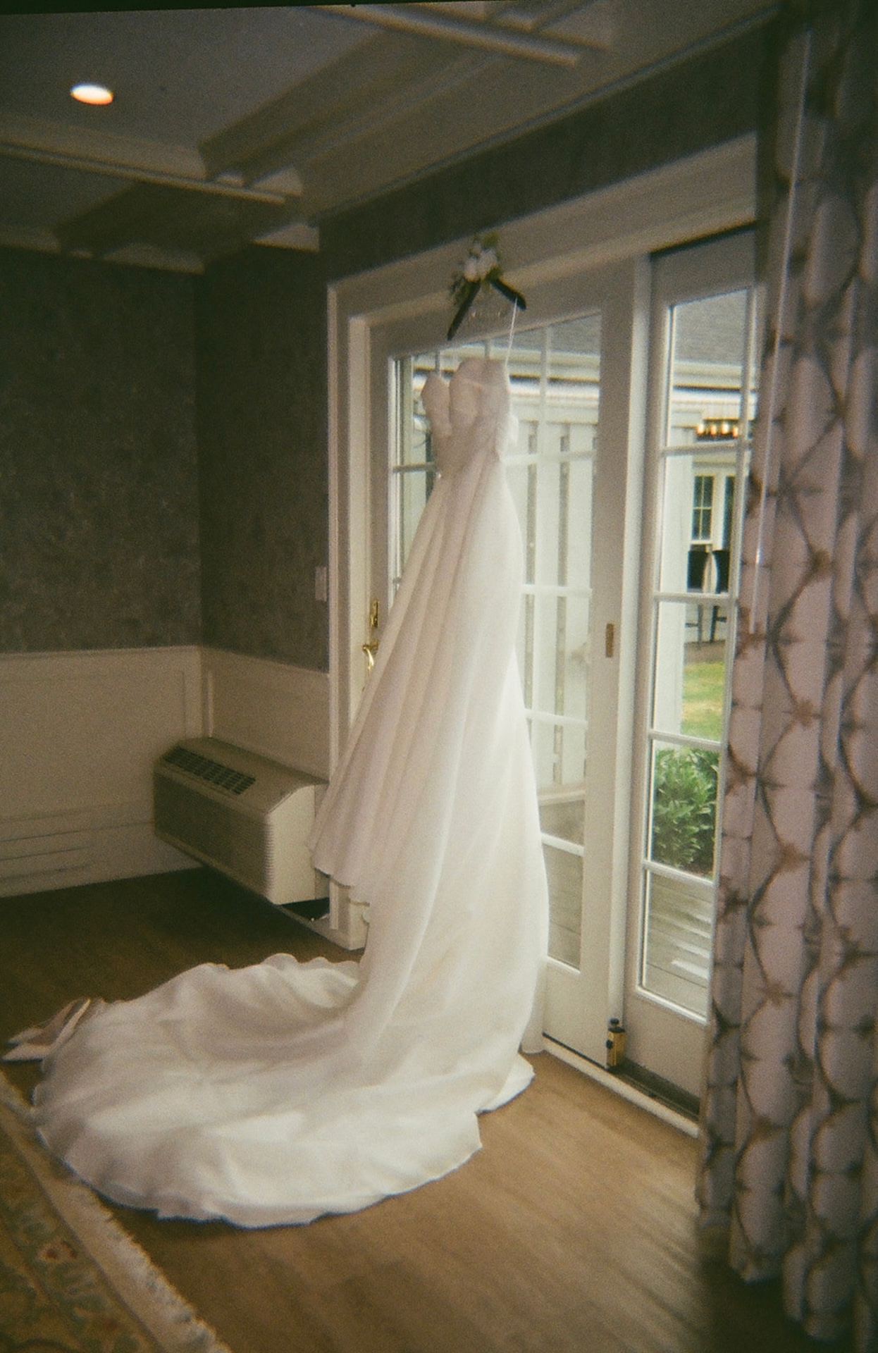 Film photo of a strapless wedding gown hanging in a window overlooking the grounds at Stage Neck Inn.