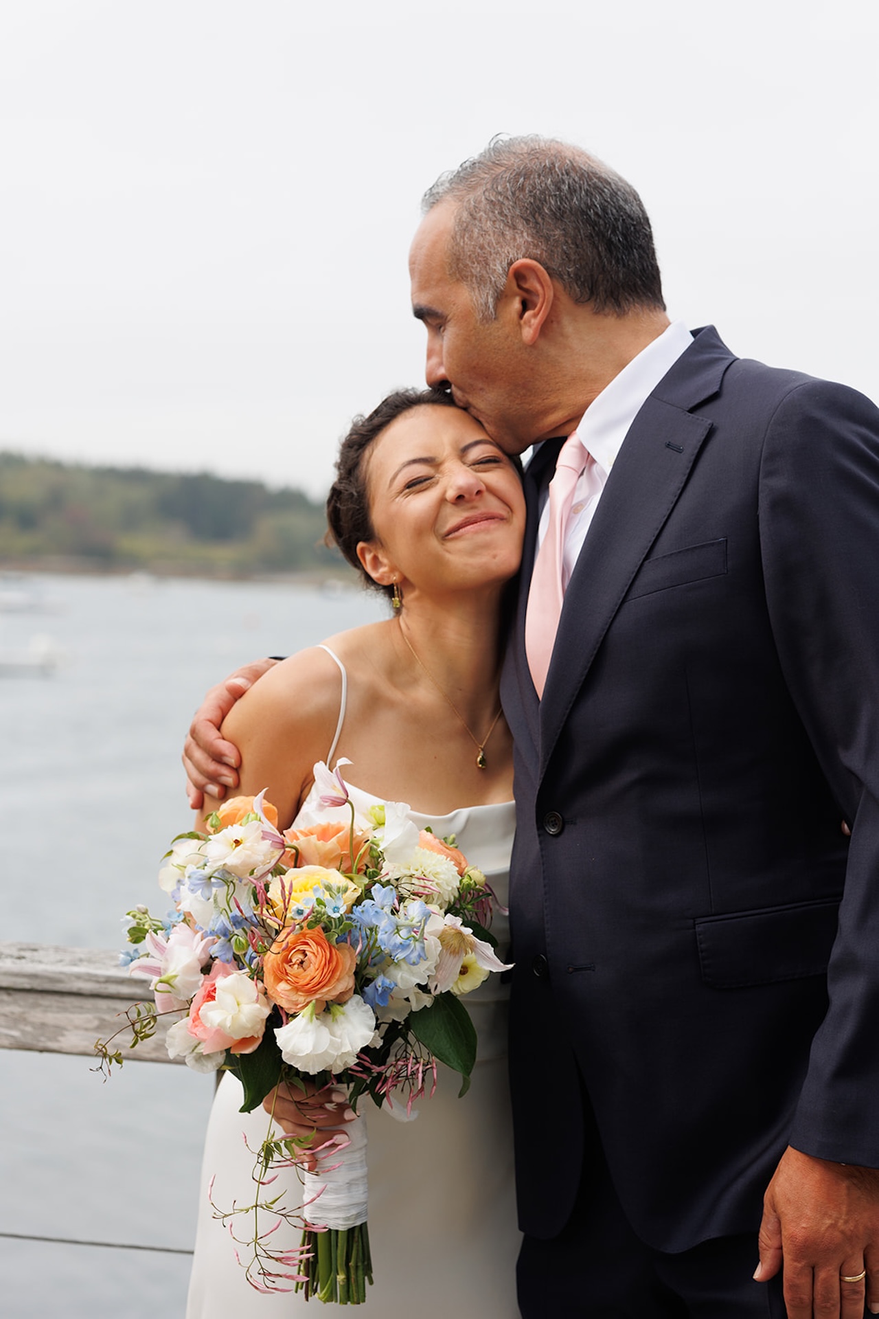A bride posing with her dad and holding bright wedding florals for her colorful wedding.