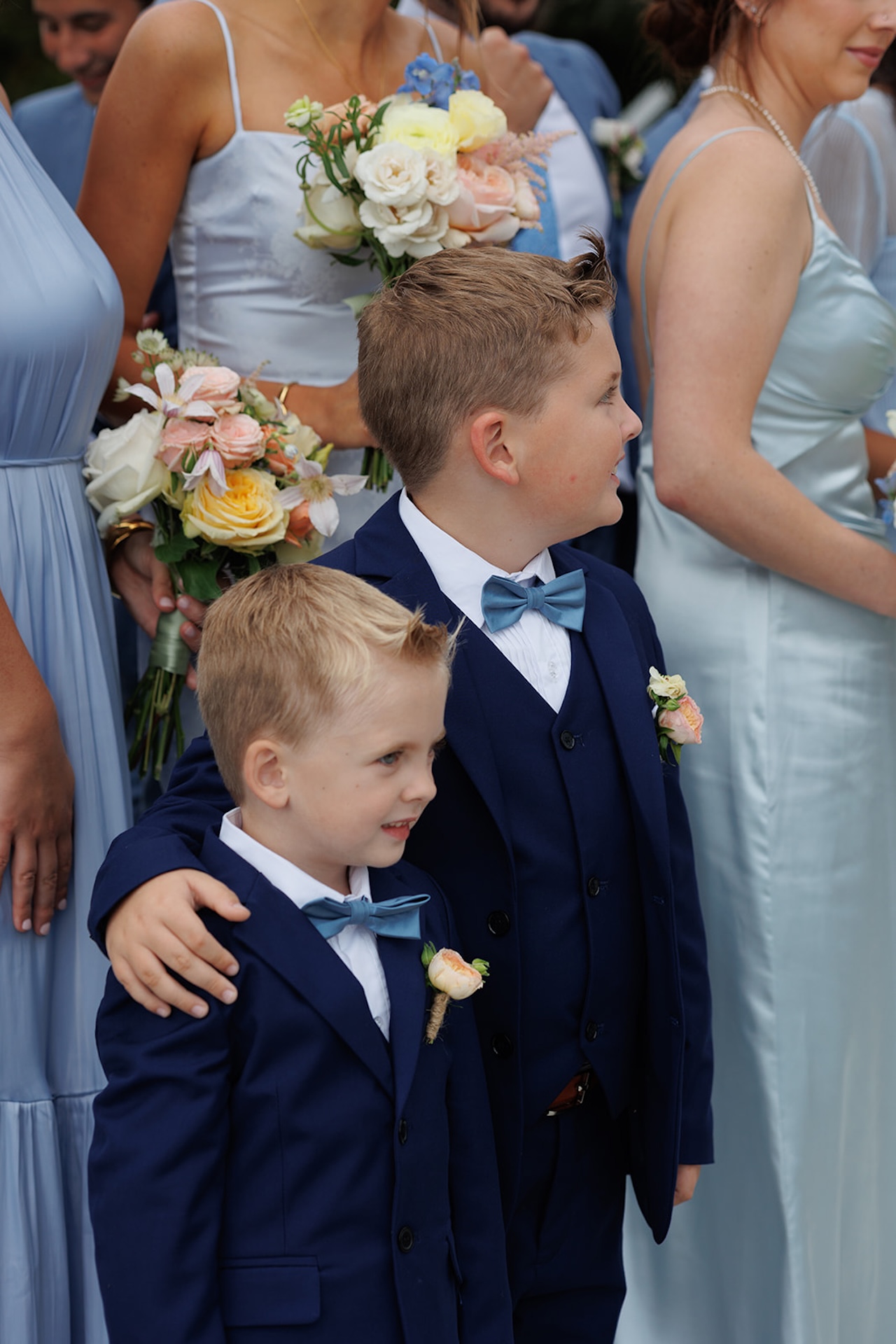 The ring bearers in blue suits with the bridesmaids in blue dress standing behind them holding bright florals.