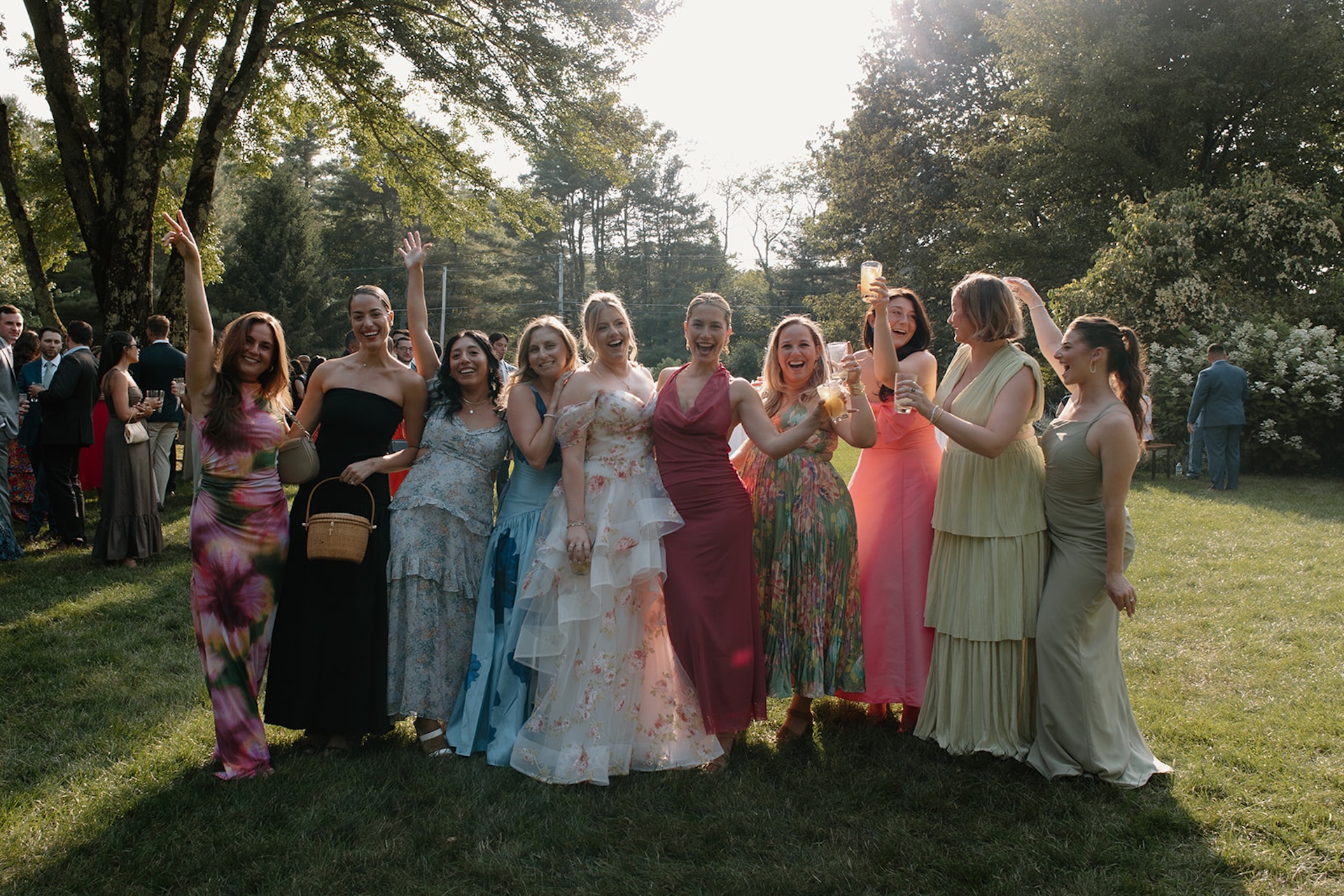 A bride standing with weddings guest, all the guests are in colorful wedding guest dresses.