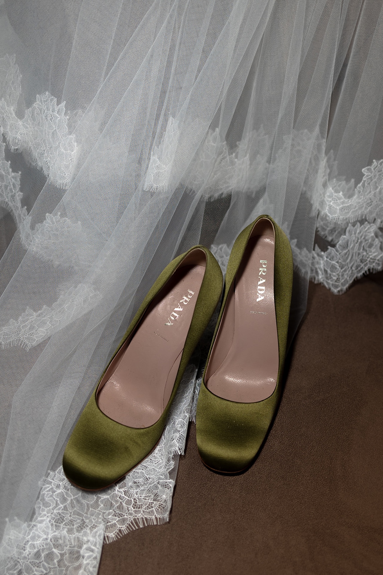 A flash detail photo of the brides dress and green satin shoes laying on top of her veil.