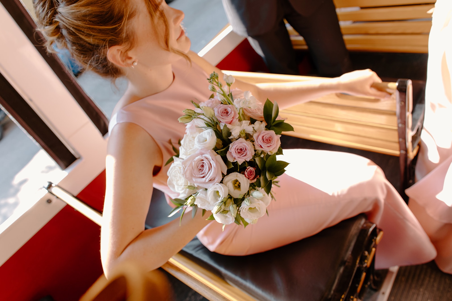 A bridesmaid in a pink dress holding a pastel pink and white wedding bouquet.
