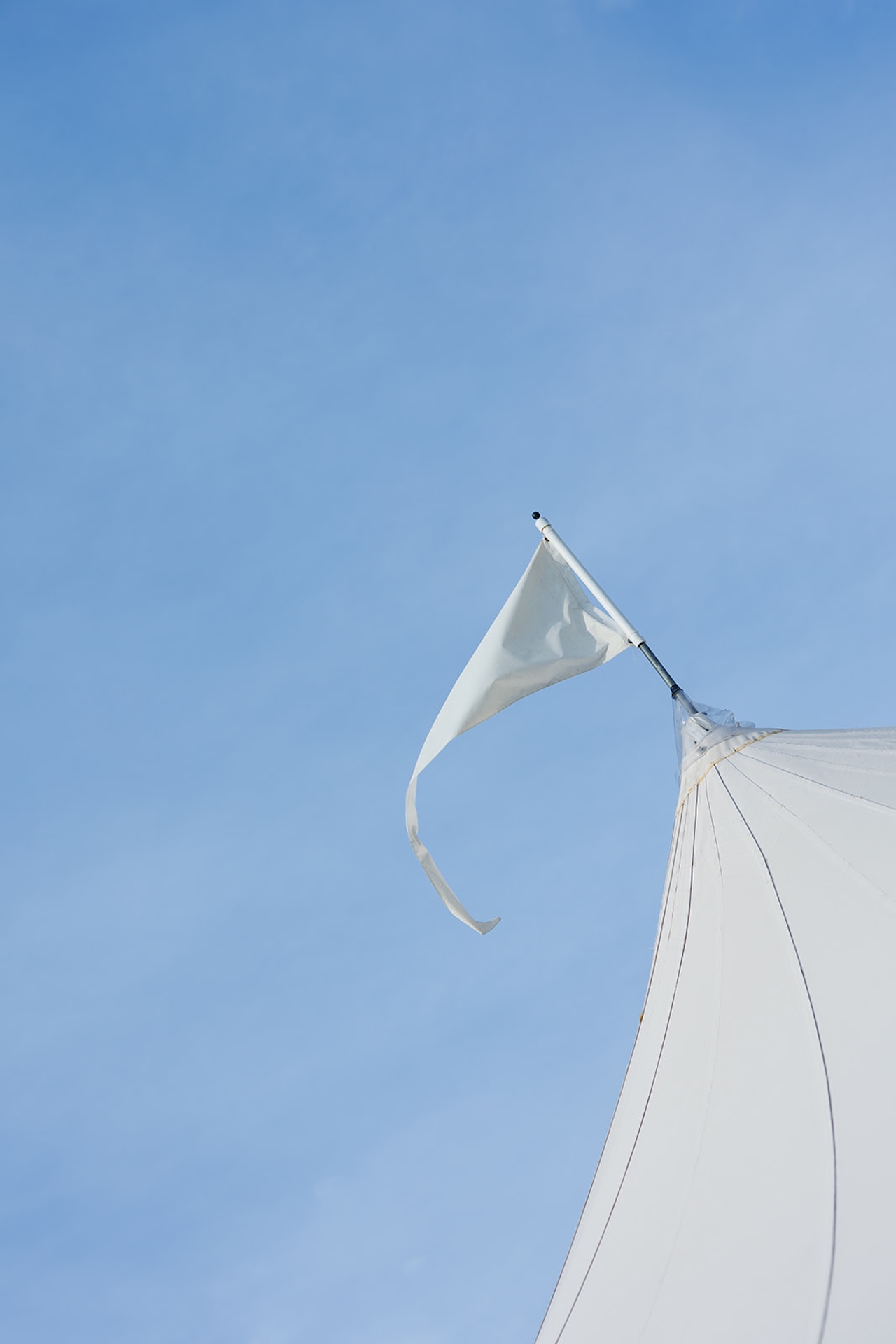 A detail photo of the flag on top of a white wedding venue tent with the bright blue sky behind it.