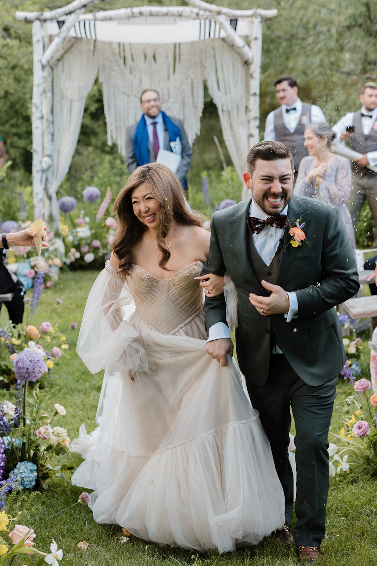 A bride and groom smiling and walking down the aisle with colorful florals decorating the aisle for their colorful wedding.