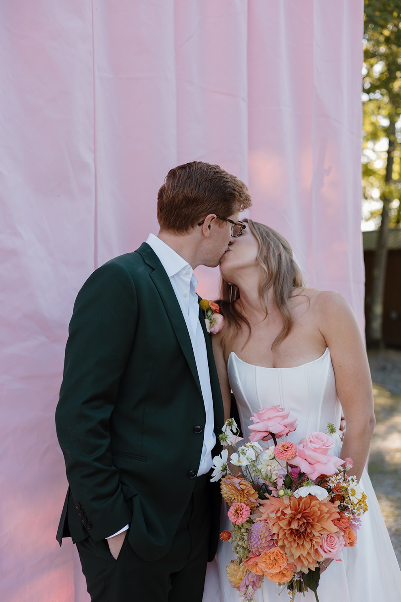 Bride and groom portraits with the bride holding a colorful bouquet with bright pinks, oranges, yellows, and purples with a bright pink backdrop behind them. Perfect inspiration for colorful weddings.