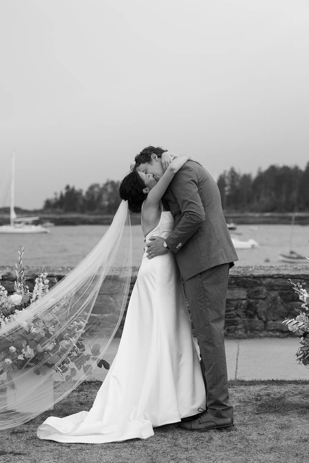 Bride and groom kissing after their coastal Maine micro wedding ceremony with sailboats in the background.