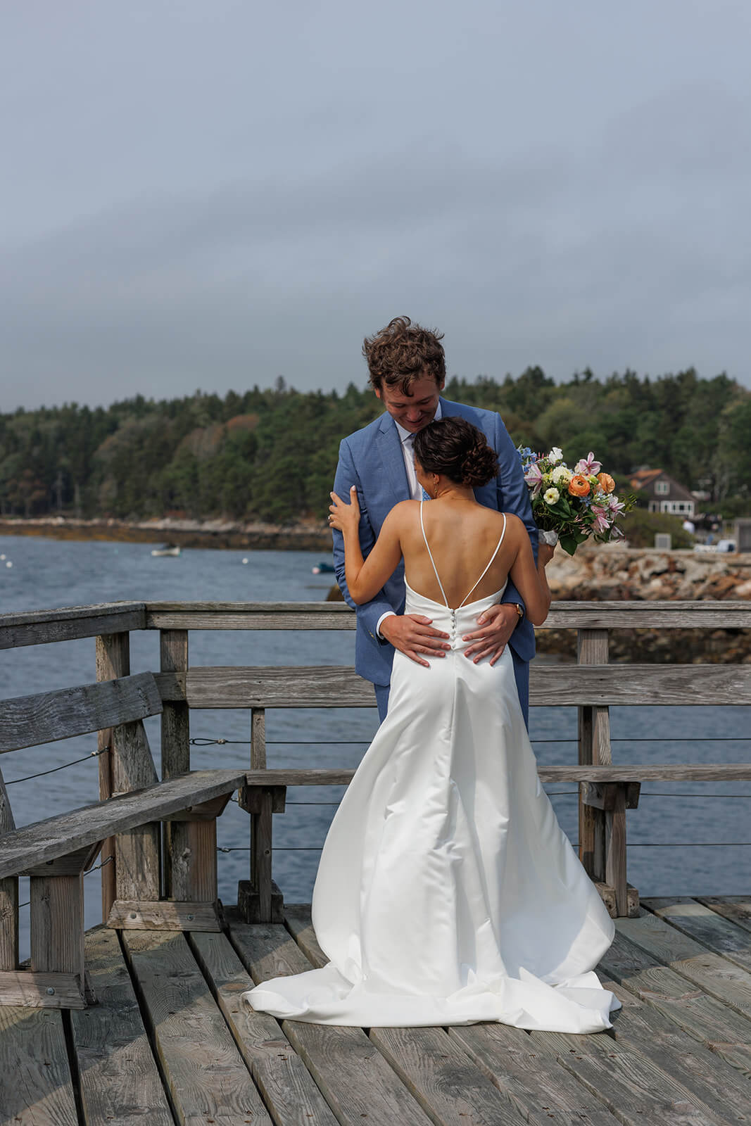 Bride and groom embracing on a wooden dock during their coastal Maine micro wedding portraits.