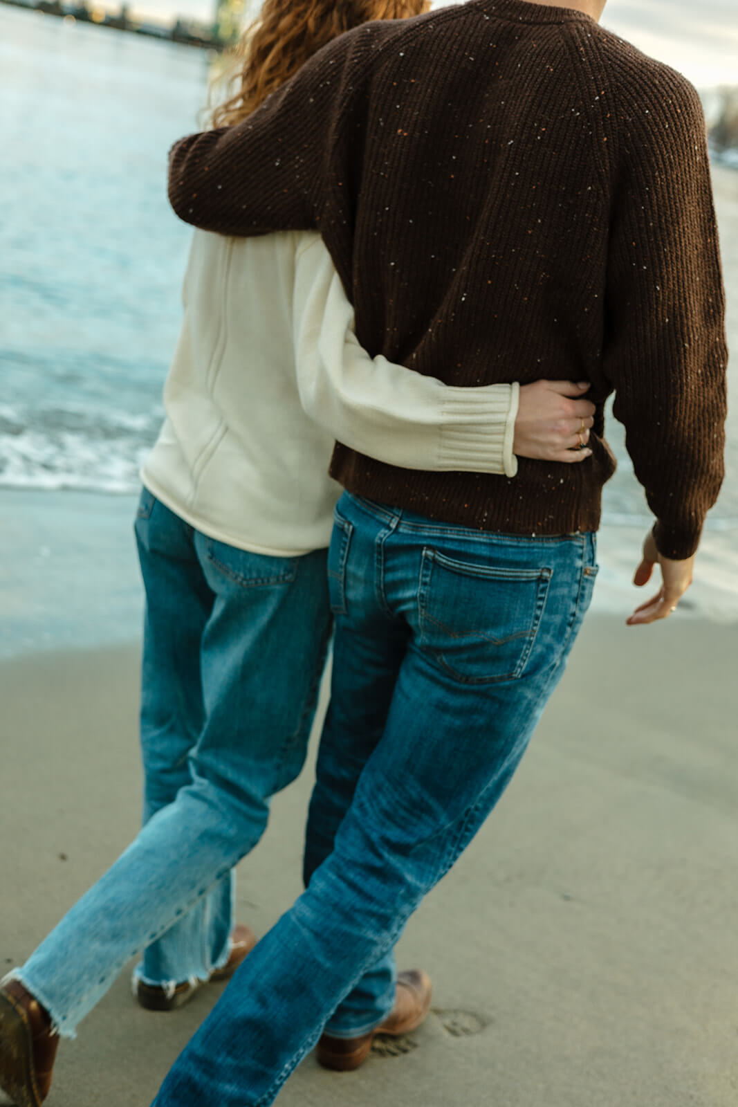 Candid engagement photoshoot image of a couple walking barefoot along the shoreline together