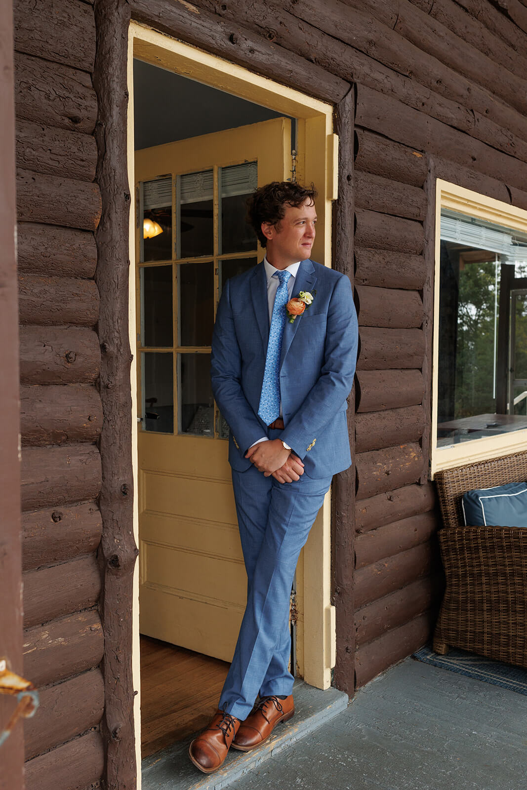 Groom in blue suit standing in the doorway of a rustic coastal Maine wedding venue before the ceremony.


