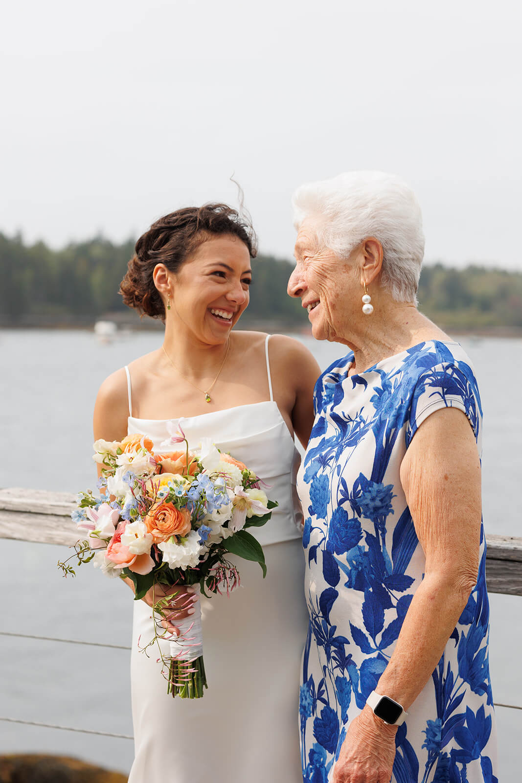 Bride sharing a joyful moment with her grandmother during a waterfront wedding in coastal Maine.