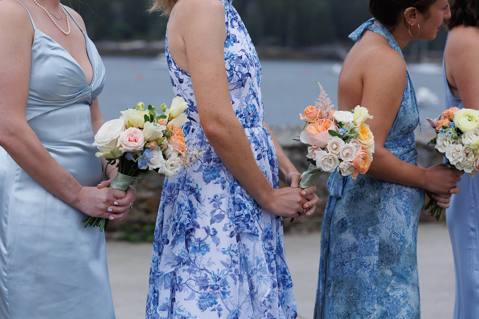 Bridesmaids holding pastel floral bouquets during a waterfront micro wedding ceremony in Maine.