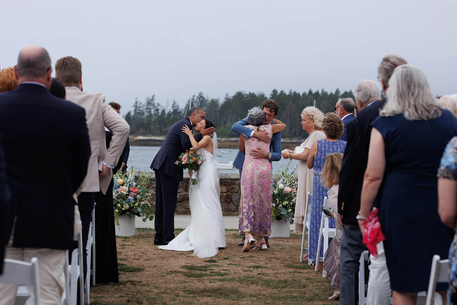 Newly married couple hugging family members after their coastal Maine wedding ceremony by the water.