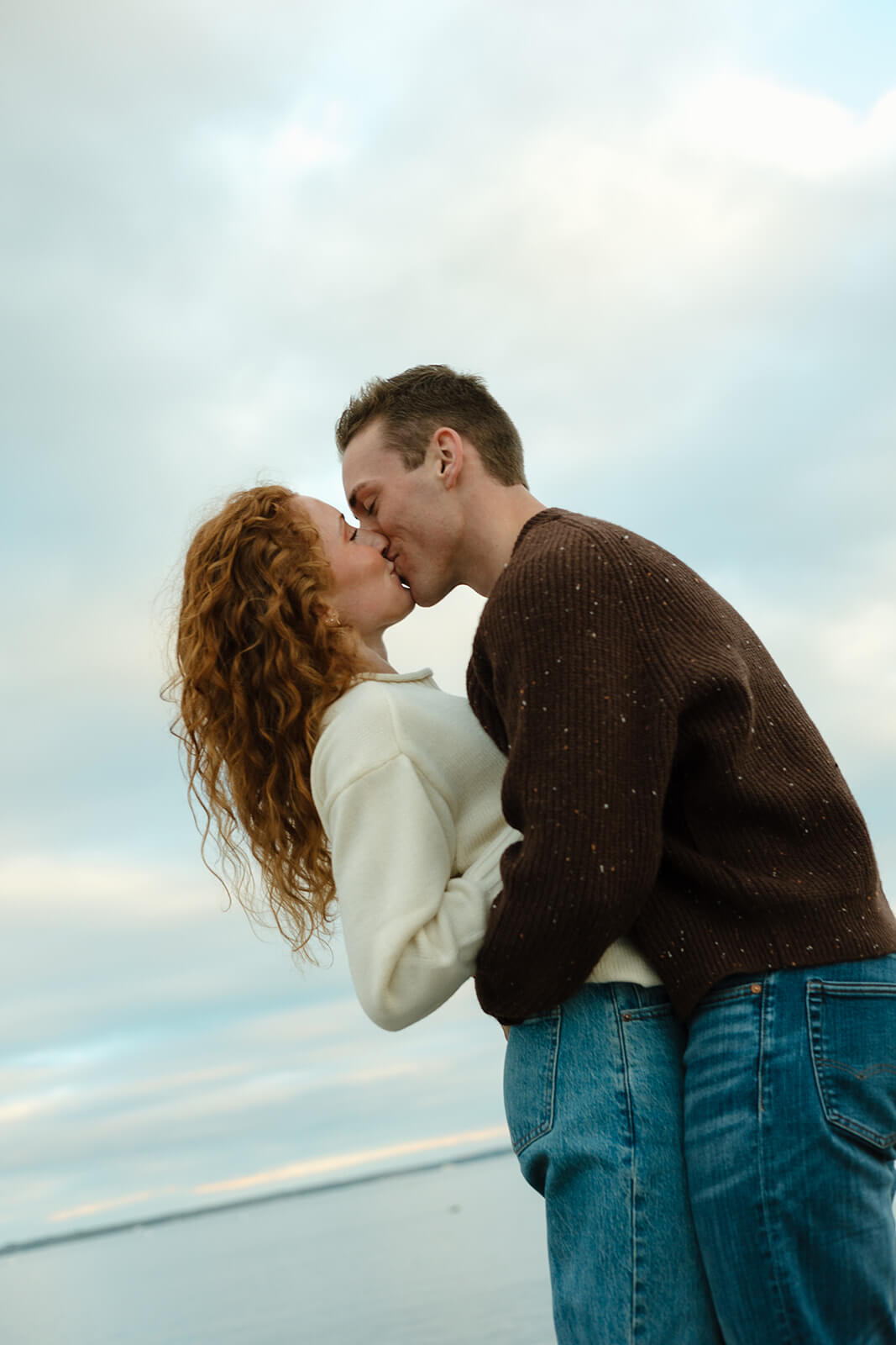 Romantic beach engagement photoshoot portrait of a couple kissing at sunset along the Maine coastline