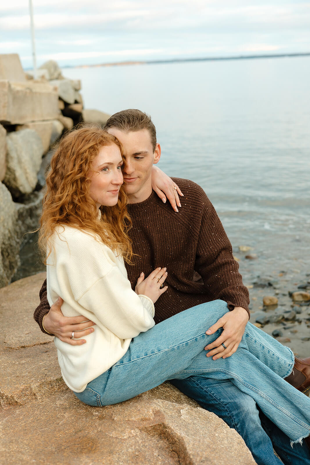 Romantic engagement photoshoot portrait of a couple cuddling on seaside rocks by the ocean