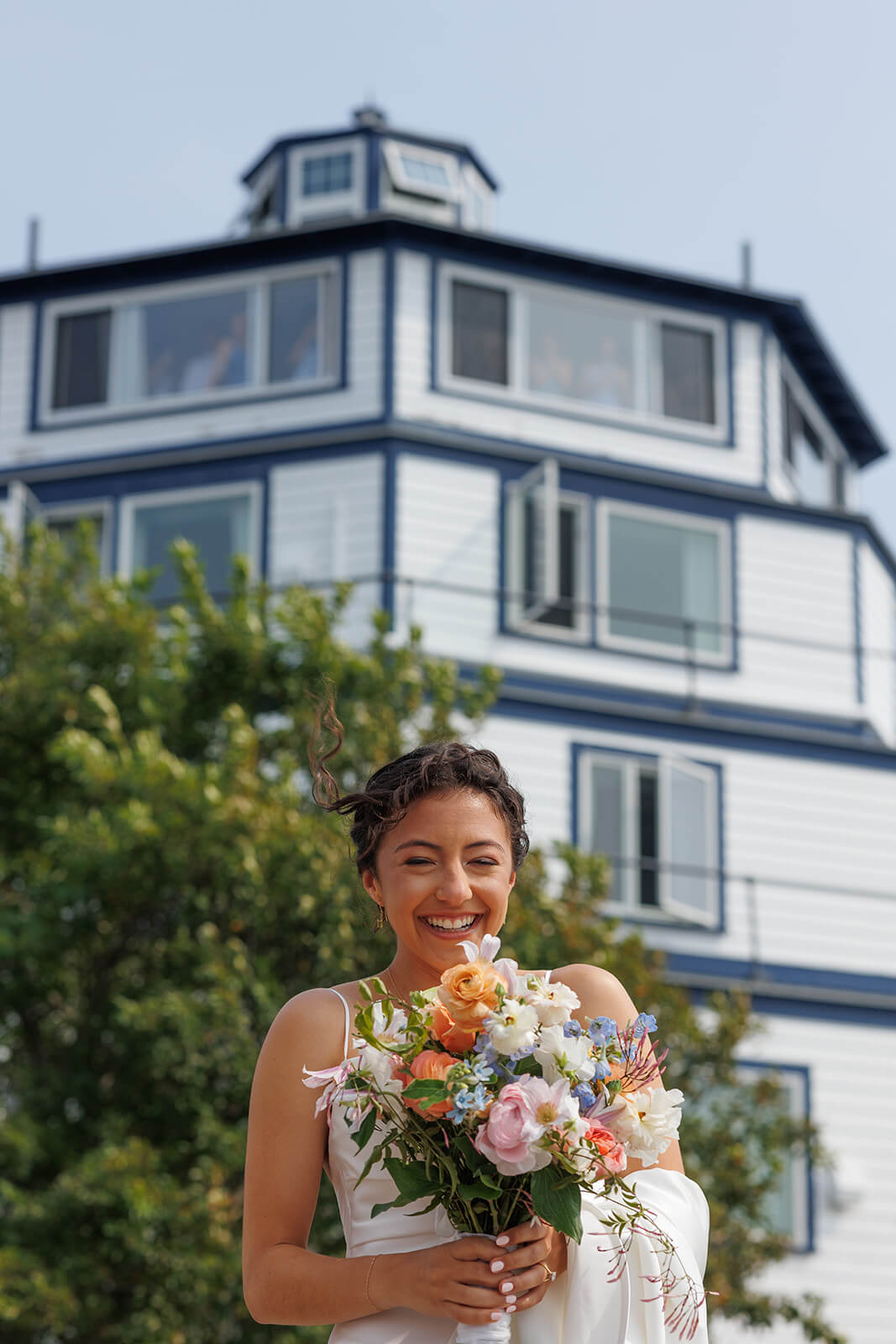 Bride smiling with bouquet outside a coastal Maine micro wedding venue on a sunny summer afternoon.