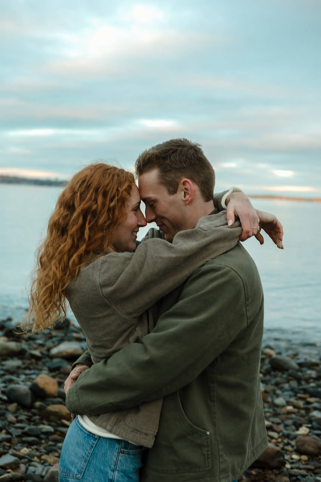 Romantic engagement photoshoot portrait of a couple hugging on a rocky beach in coastal Maine