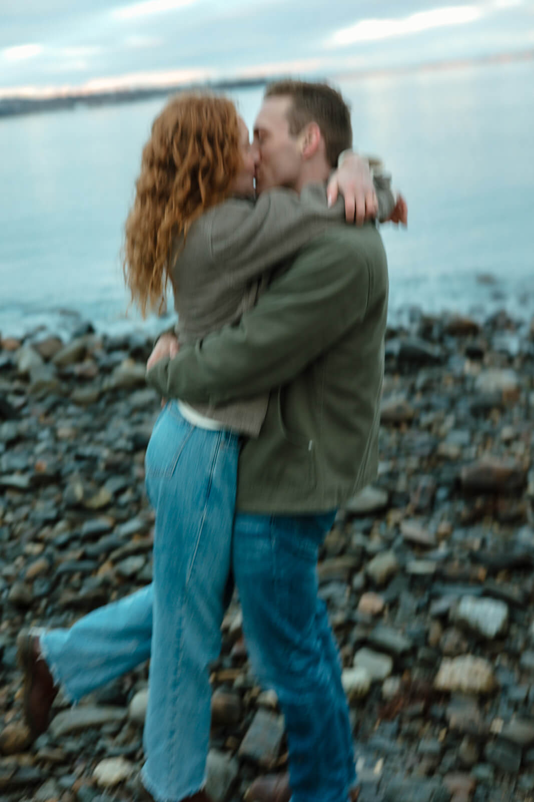 Motion blur engagement photoshoot image of a couple kissing on a rocky beach in Maine