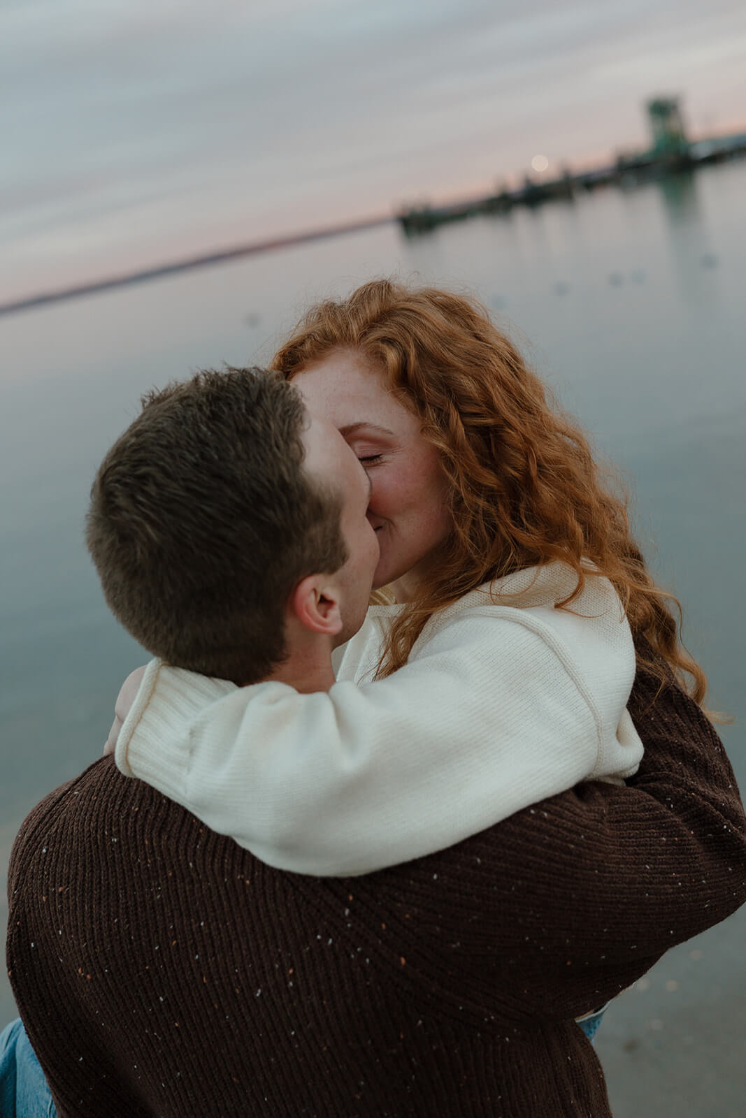Romantic coastal engagement photoshoot portrait of a couple embracing and kissing by the ocean at sunset in Maine