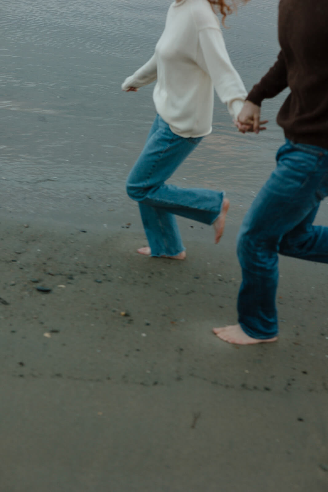 Couple running barefoot hand-in-hand during a fun coastal Maine engagement photoshoot