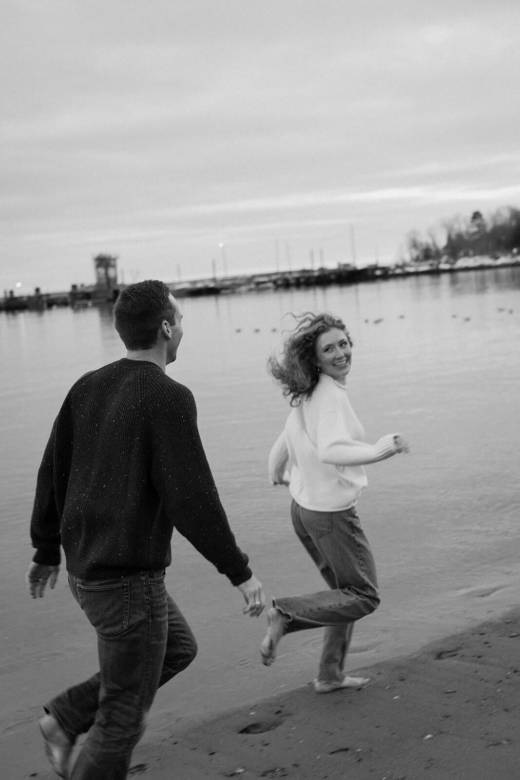 Black and white engagement photoshoot image of a couple running along a quiet Maine beach