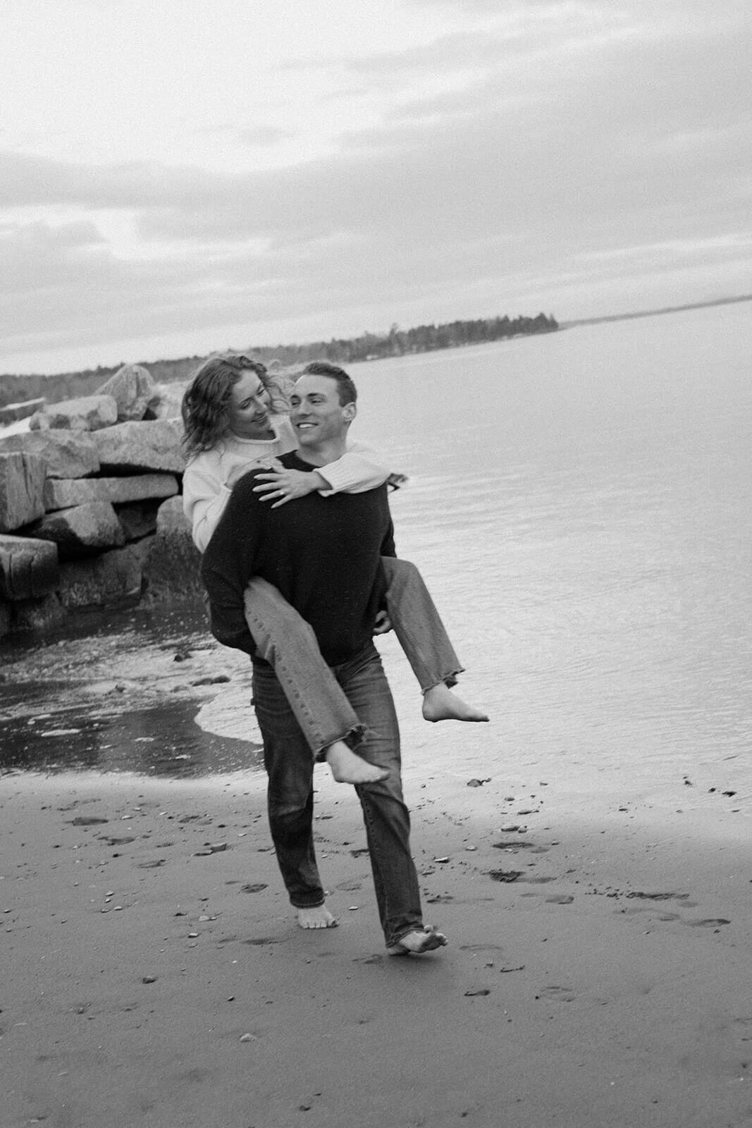 Playful engagement photoshoot image of a woman running barefoot along the shoreline in coastal Maine