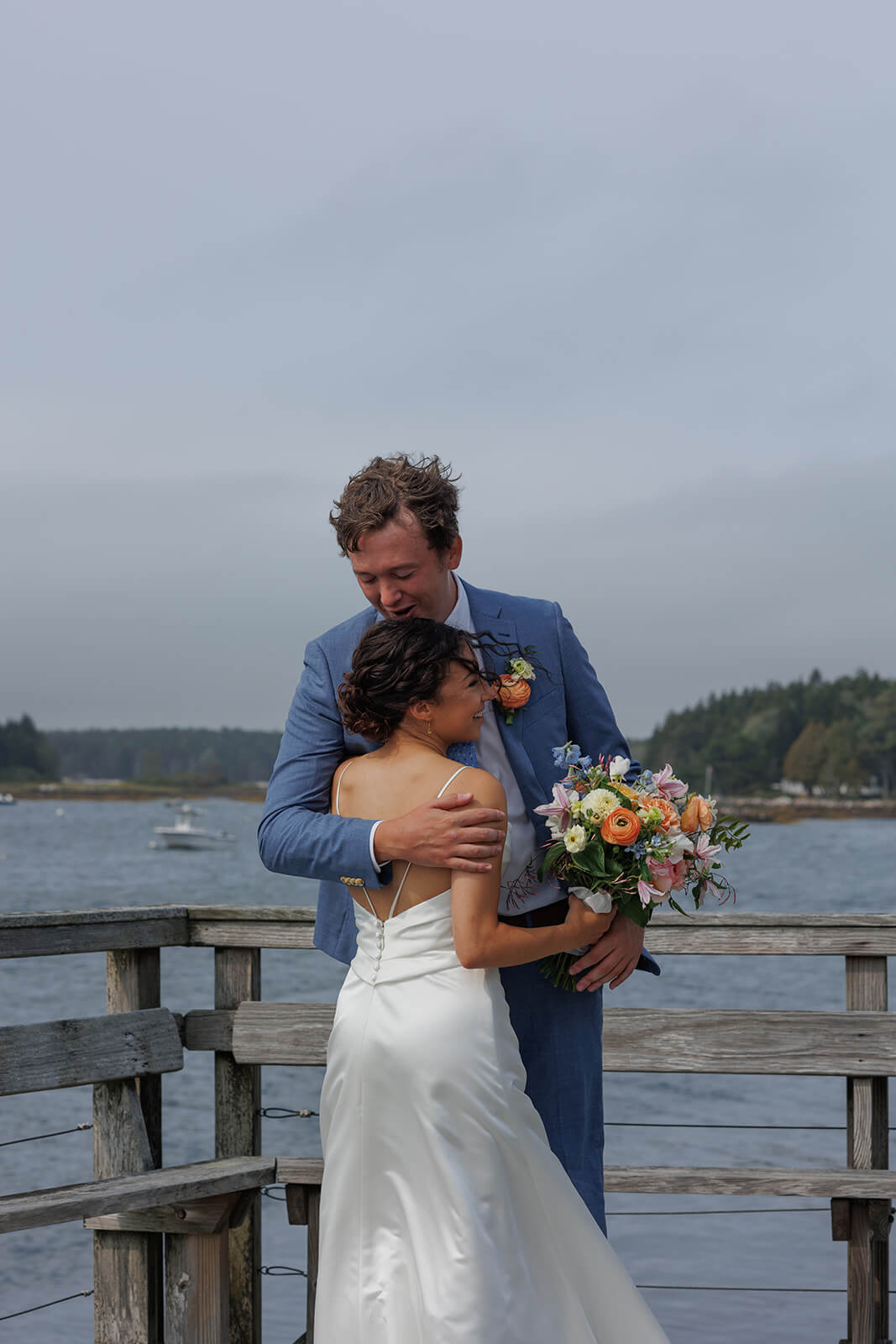 Romantic waterfront portrait of a bride and groom embracing during their coastal Maine micro wedding.

