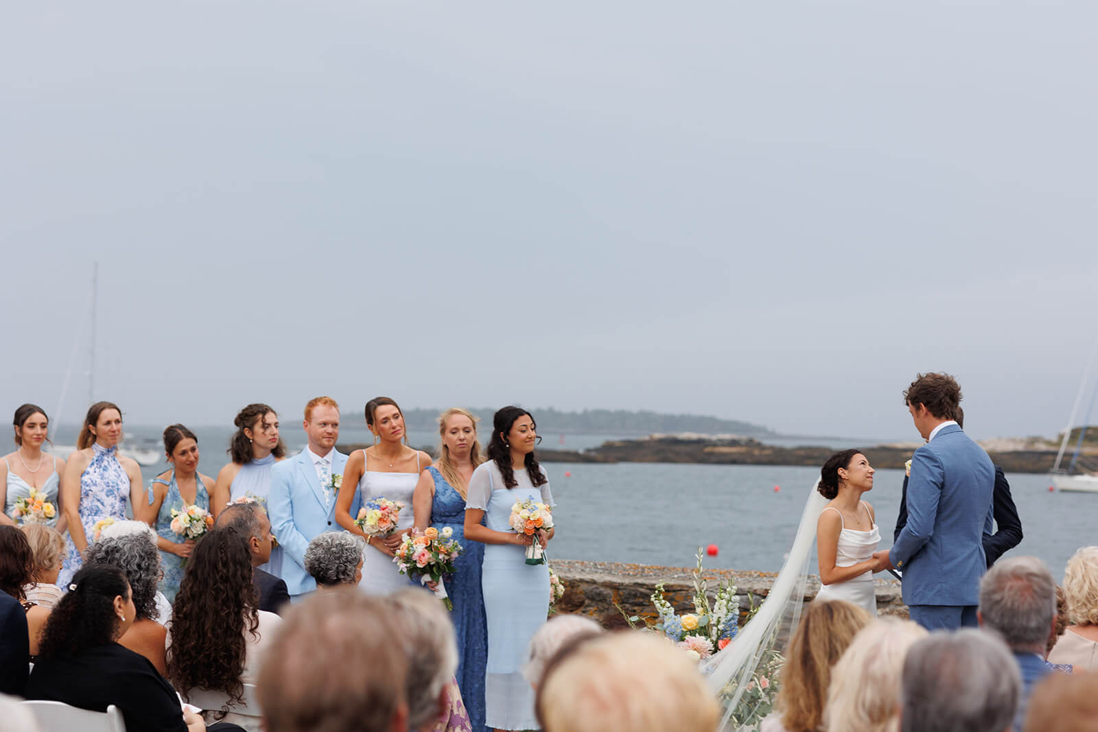 Waterfront micro wedding ceremony in coastal Maine with bridesmaids standing beside the couple.
