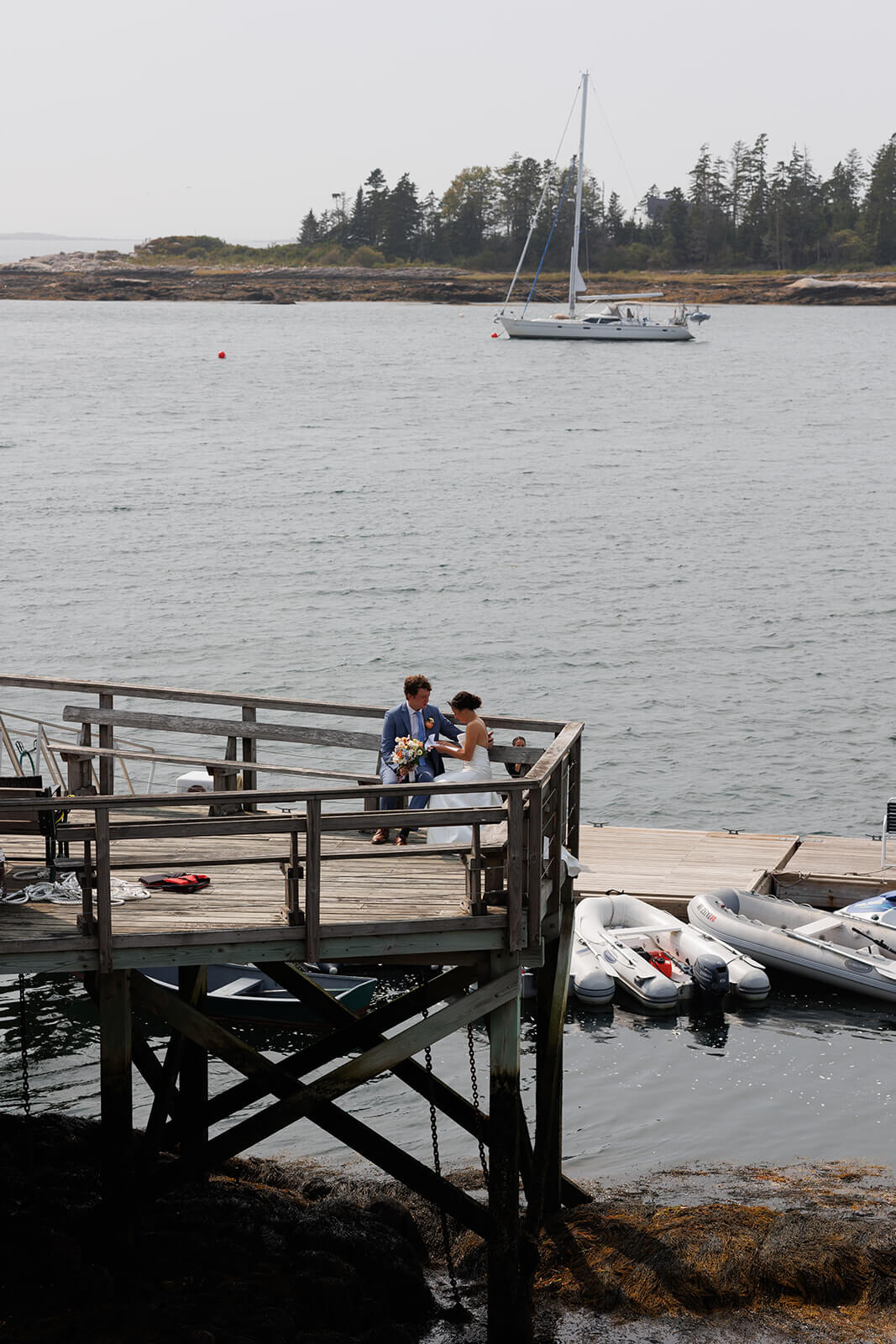 Wide view of bride and groom sharing a quiet moment on a waterfront dock during their coastal Maine micro wedding.

