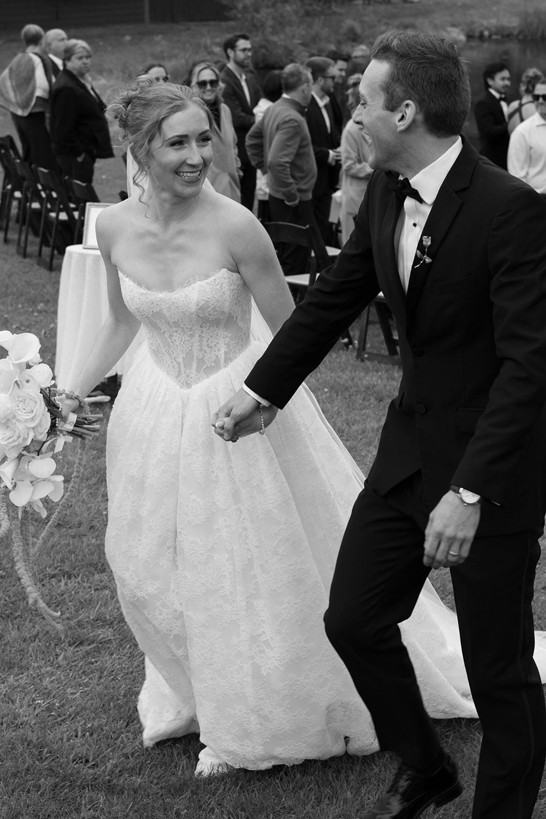 Black-and-white photo of the newlyweds laughing and holding hands after their outdoor wedding ceremony.