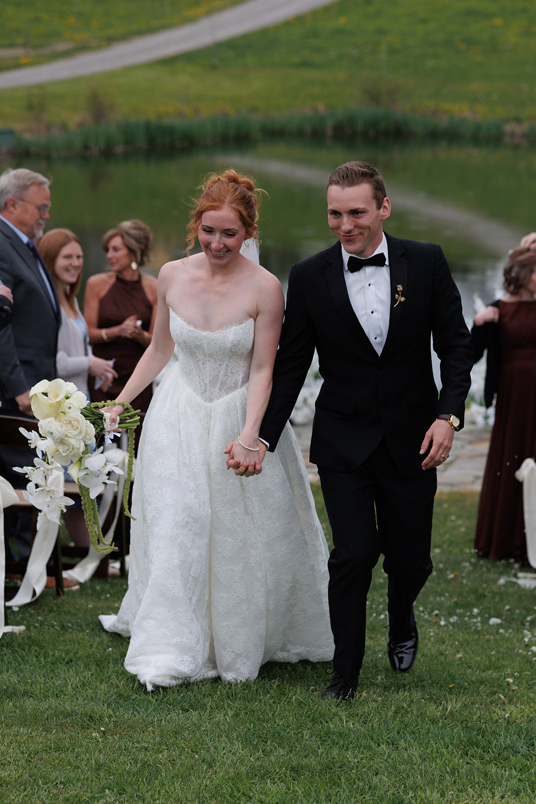 Newlyweds smiling and walking away from their pondside wedding ceremony while holding hands.