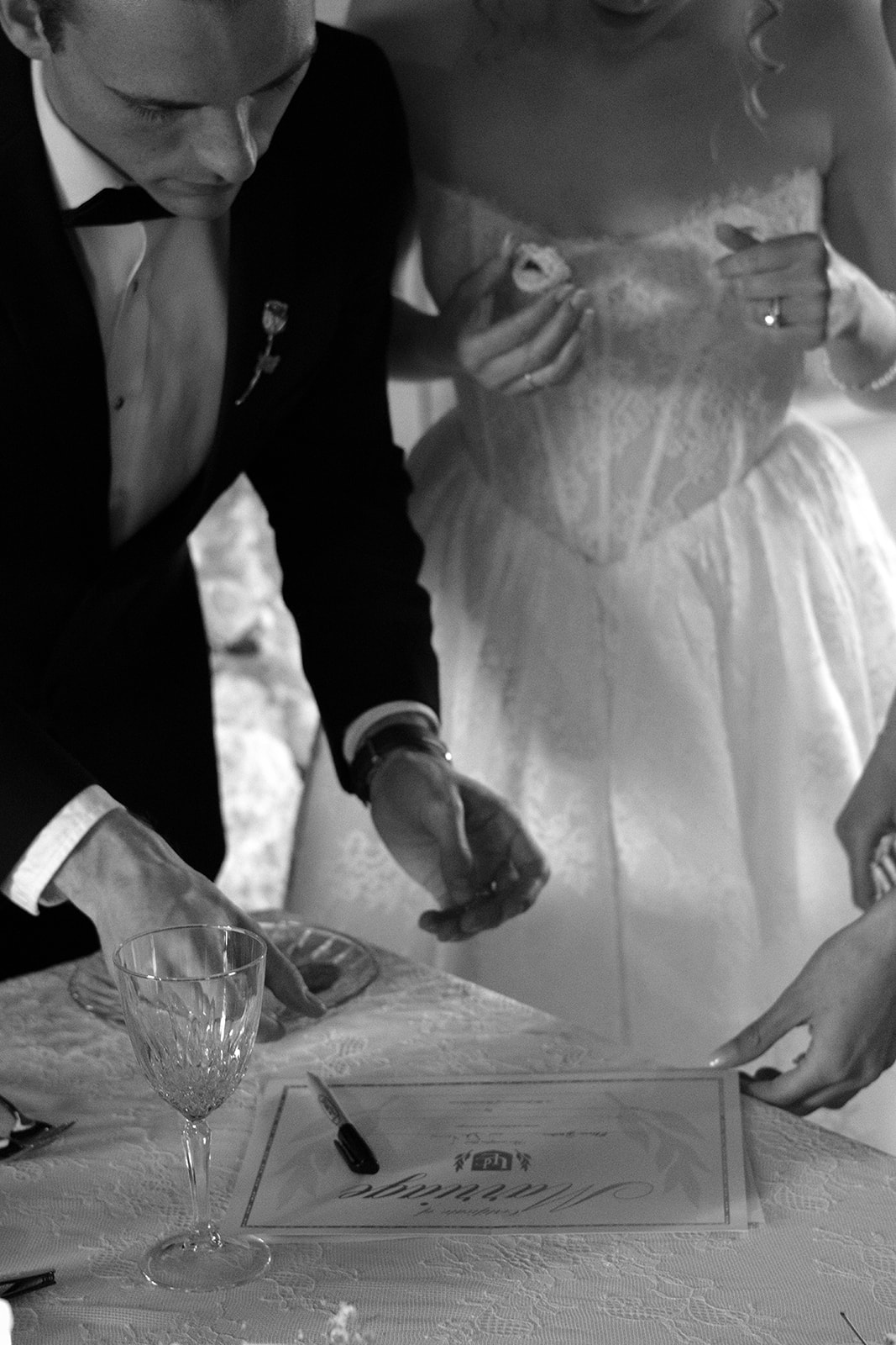 Black-and-white photo of the bride and groom signing their marriage certificate at a reception table.