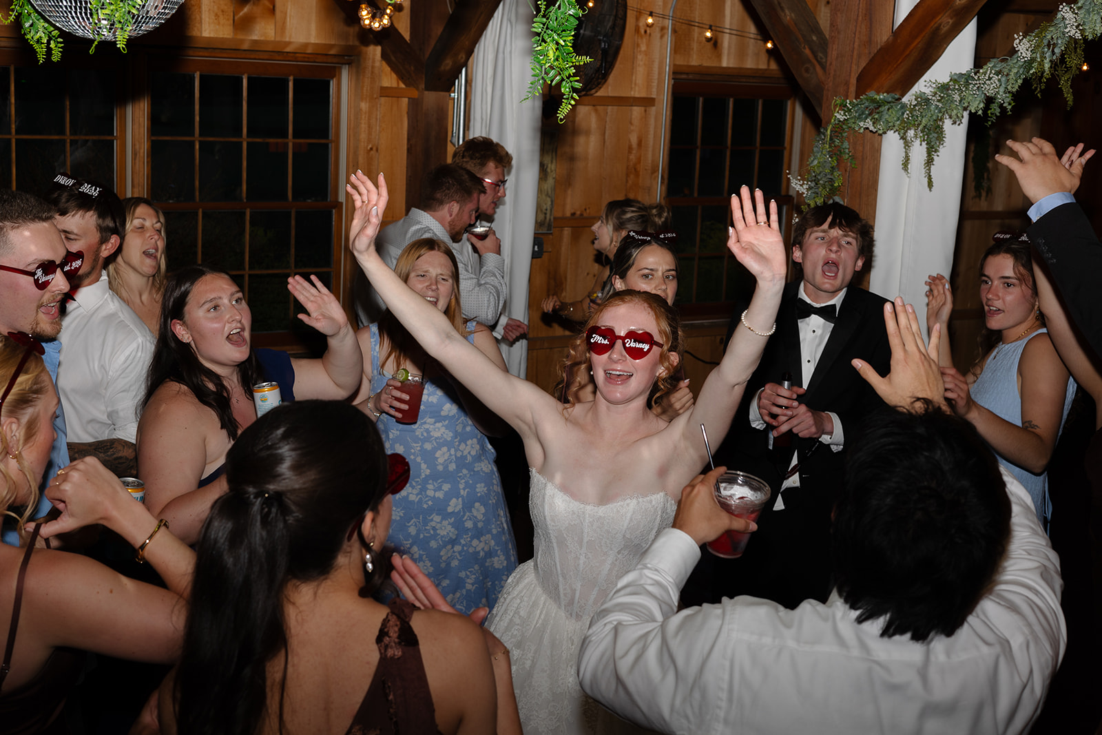 Bride dancing with her arms raised among guests during a lively barn wedding reception.
