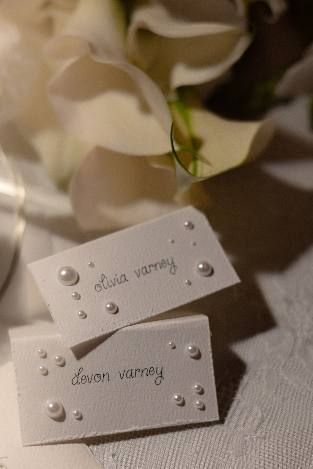 Pearl-decorated wedding place cards displaying the names Olivia Varney and Devon Varney beside white flowers.