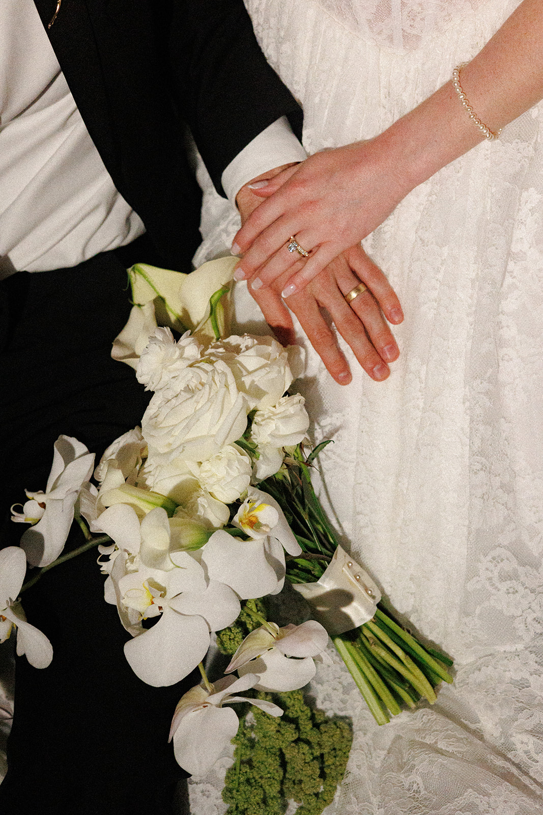 Close-up of the newlyweds holding hands above the bride’s cascading white orchid bouquet.