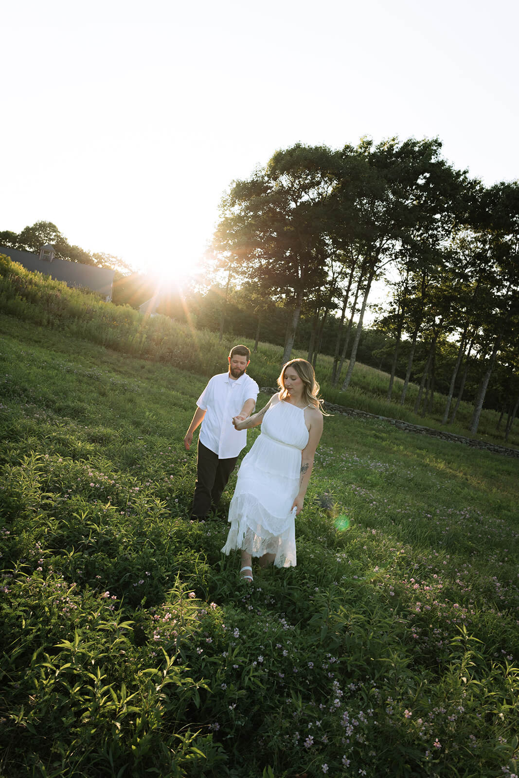 Couple walking hand in hand through a wildflower field at sunset at Beech Hill Barn in Pittston, Maine.