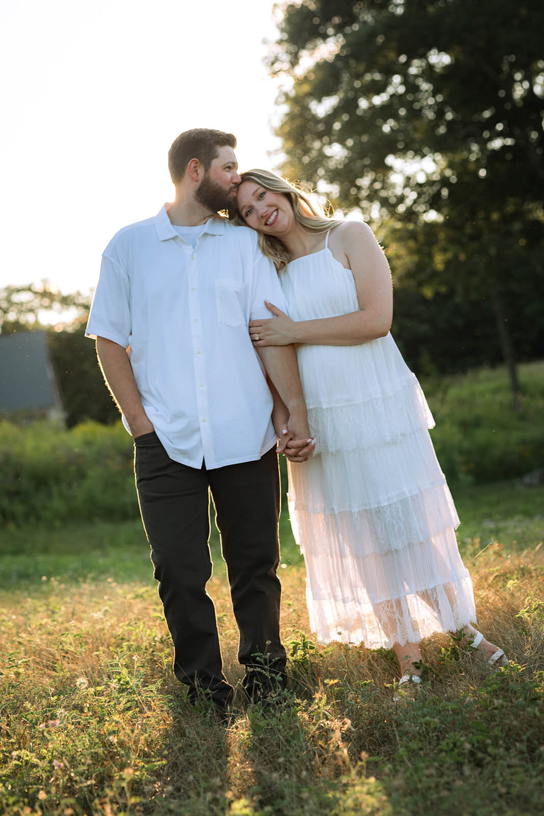 Man kissing the top of his partner’s head as they stand holding hands together in the evening light at Beech Hill Barn.