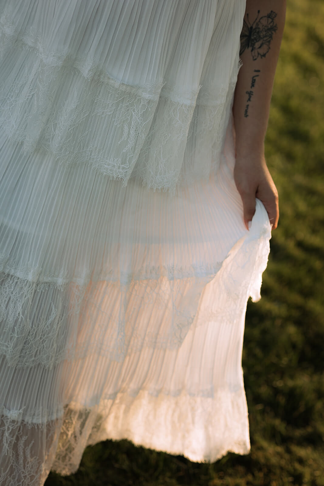 Close-up of the layered lace and pleated skirt of a white dress glowing in the evening sunlight.