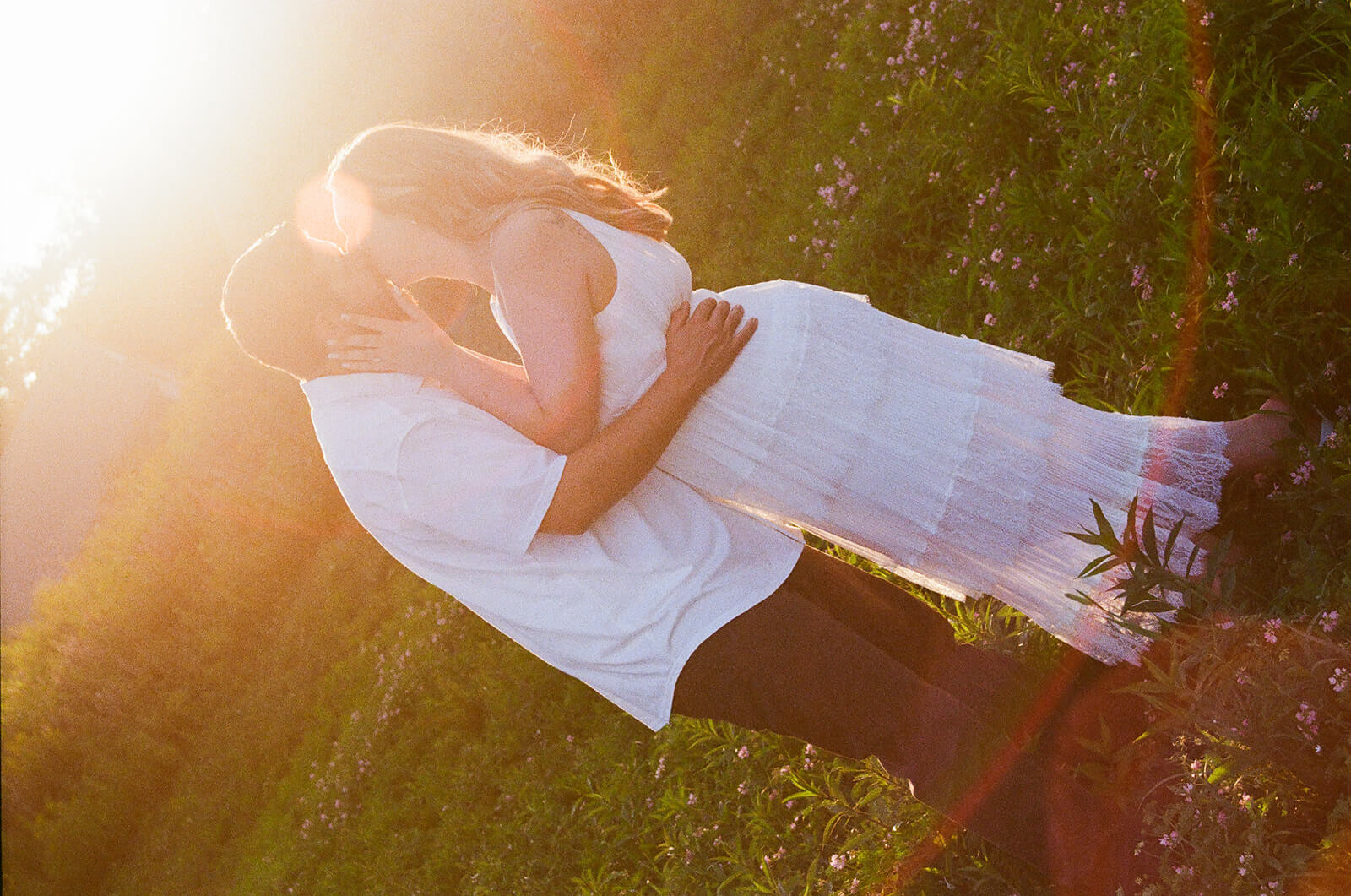 Couple kissing in a grassy wildflower field with bright golden sun flare behind them at Beech Hill Barn.