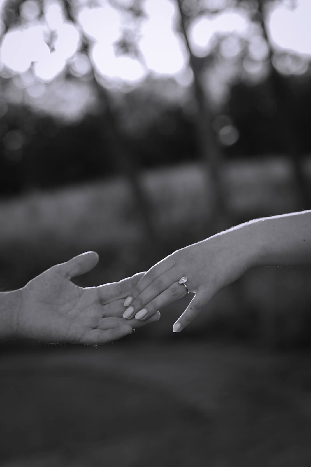 Black-and-white close-up of a couple reaching their hands toward each other with the woman’s engagement ring visible.