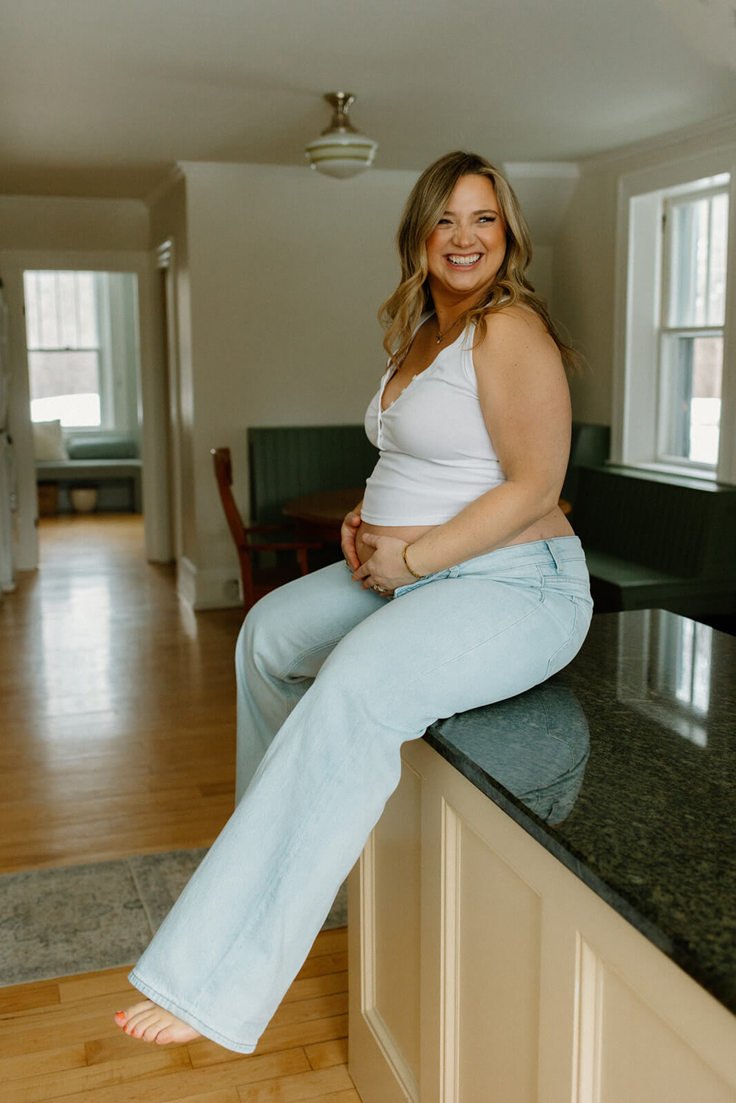 Maternity photoshoot at home portrait of an expecting mother smiling while sitting barefoot on the kitchen counter.