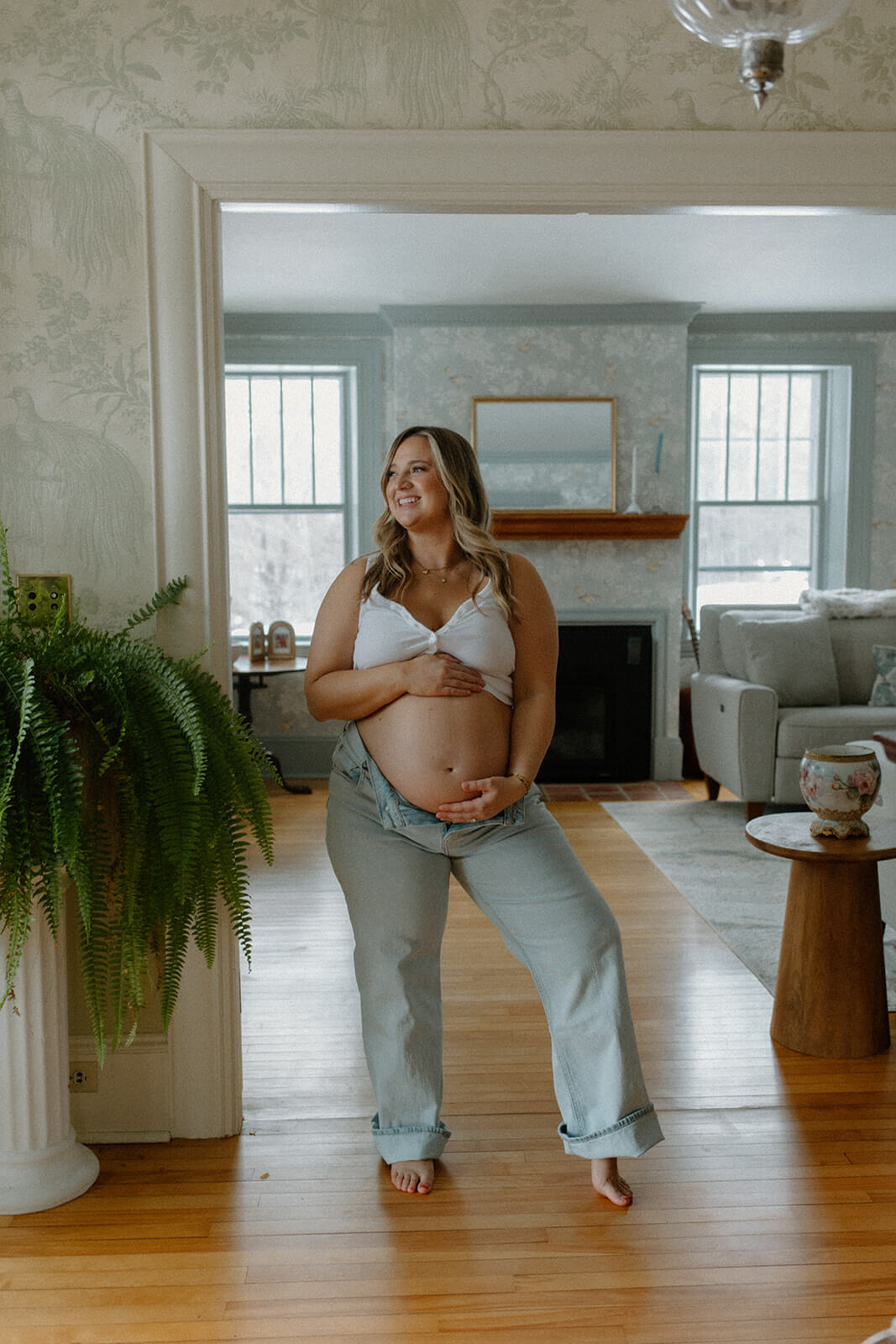 Maternity photoshoot at home of an expecting mother standing in a doorway and smiling while holding her bare belly.